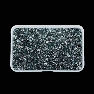 Macro view of irregular glossy teal glass crushed stones in a plastic storage box.