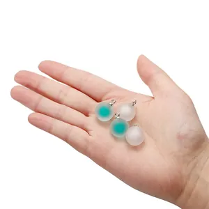 Macro detail of frosted acrylic ball charms with metal loops held in palm for scale
