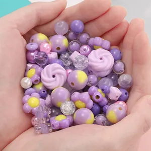 Primo piano di perle fai da te viola e gialle per gioielli tenute in mano.