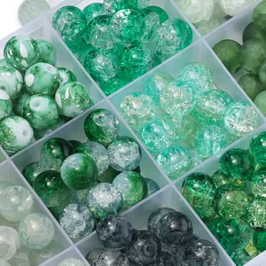 Macro view of assorted green crackle and frosted glass beads in a storage organizer box.