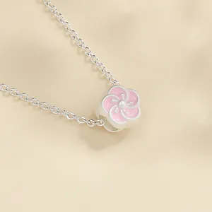 Primo piano di un ciondolo rosa a fiore di prugno su una collana d'argento opaco.