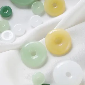Makroansicht bunter Glas-Imitat-Jade-Donut-Perlen auf weißer Seide.
