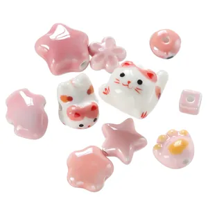 Close-up of pink and white ceramic beads in cat, star, and paw shapes with glossy finish.