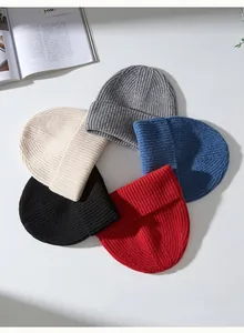 Bonnets en pure laine tricotés aux couleurs vives disposés sur une surface blanche unie.