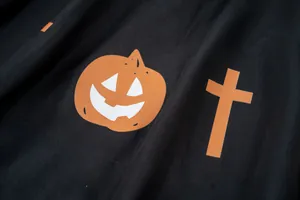Vista dettagliata della mantella nera di Halloween per animali con zucca e croce arancio.