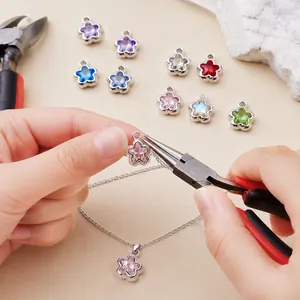 Mains utilisant une pince pour fixer une fleur rose à une chaîne de collier.