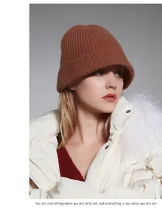 Detail of a brown wool knit fisherman hat worn by a model in a white jacket.