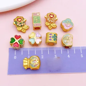 Detail view of golden alloy spacer beads with Chinese motifs next to a centimeter ruler.