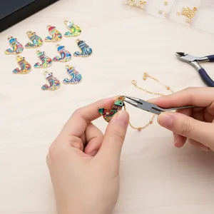 Close-up of hands using pliers to attach a colorful enamel bird charm to a gold chain.
