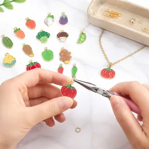 Detailed view of handmade vegetable enamel charm assembly using professional pliers