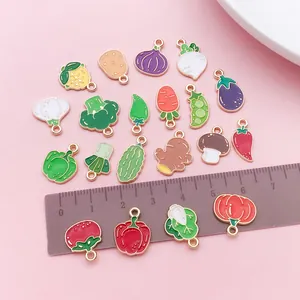 Close-up of various vegetable enamel charms with a brown ruler for size comparison.