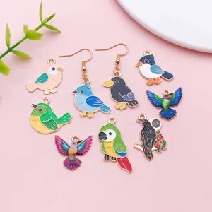 Détail de breloques et boucles d'oreilles oiseaux en émail sur fond rose