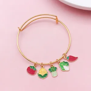 Close-up of enamel vegetable charms including tomato and corn on a gold-tone bangle.
