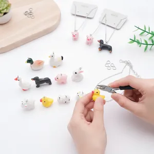Handen die met een tang een kleine gele eendenhanger van hars aan een ketting maken