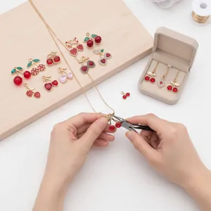 Detail shot of hands crafting a jewelry piece using red rhinestone cherry charms
