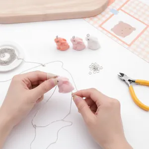 Gros plan montrant le processus DIY d'un pendentif lapin rose duveteux sur une chaîne argent