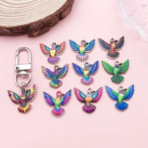 Colorful hummingbird charms and a metal keychain clasp on a soft pink background.