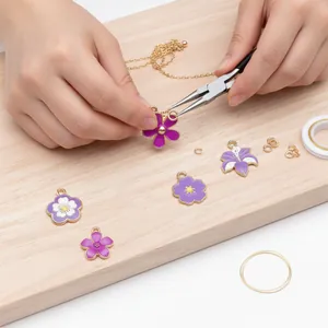 Détail de mains créant des bijoux DIY avec des breloques fleurs en émail violet