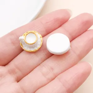 Close-up of miniature white teacup and saucer resin charms on a hand for scale.