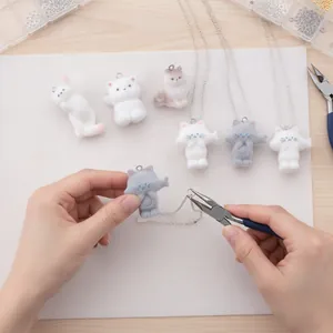 Primer plano de dijes de gato flocados DIY siendo ensamblados en un collar con colgante.