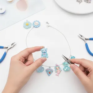 Detail of hands assembling a blue resin mermaid and bear charm necklace with tools