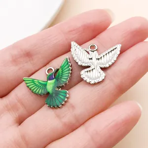 Detailed close-up of green printed and silver textured hummingbird charms on a hand