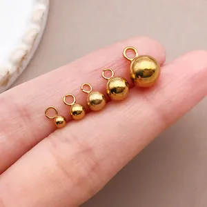 Nahaufnahme von fünf goldenen Edelstahl-Kugelanhängern in verschiedenen Größen auf Hand
