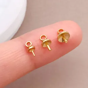 Makroaufnahme von drei vergoldeten Stiftösen für die DIY-Schmuckherstellung auf einer Fingerspitze.