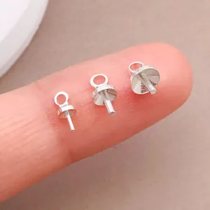 Nahaufnahme von drei silbernen Perlenkappen-Ösennadeln für DIY-Schmuck auf einem Finger.