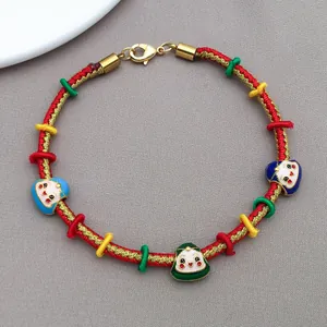 Macro shot of a handmade woven red cord bracelet featuring colorful enamel face charms