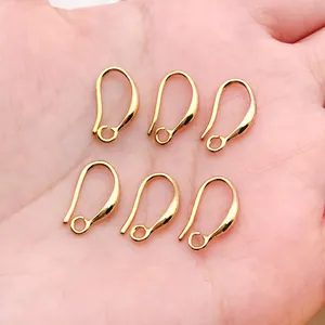 Detail view of six 18k gold-plated copper earring hooks on a neutral hand background