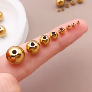 Goldene Edelstahl-Rundperlen in verschiedenen Größen auf einem Finger als Maßstab.
