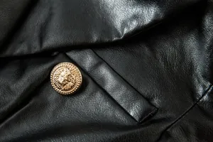 Detalle de chaqueta de cuero sintético negro con botón dorado con cabeza de león.