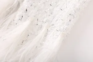 Détail macro d'une veste en tweed blanc avec paillettes argentées et plumes douces