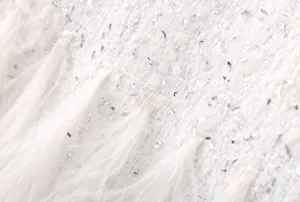 Gros plan sur un tissu en tweed blanc avec des paillettes argentées et des plumes douces