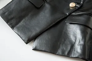 Detalle de cerca del botón dorado con cabeza de león en blazer negro de cuero sintético
