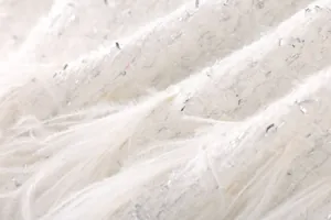 Gros plan sur un tissu en tweed blanc avec plumes d'autruche et paillettes argentées.