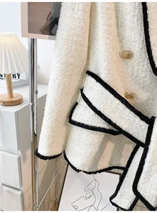 Close-up detail of an elegant white tweed jacket with gold buttons and black fringe trim.