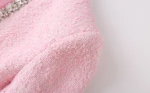 Close-up detail of pink tweed fabric texture with decorative rhinestone trim on suit