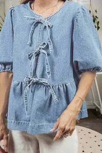 Dettaglio di una camicetta in denim azzurro con lacci frontali e maniche a sbuffo.