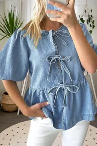 Dettaglio di camicetta in denim azzurro con fiocchi sul davanti e maniche a sbuffo