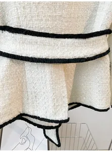 Macro view of white tweed jacket featuring elegant black fringe trim and waist belt detail.
