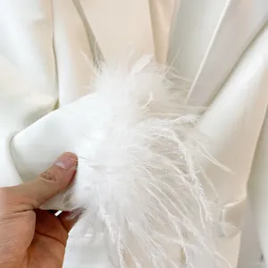 Close-up detail of white blazer sleeve featuring elegant fluffy feather trim decoration