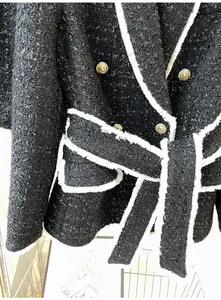 Close-up detail of black tweed jacket featuring gold lion head buttons and white fringe