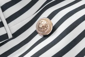 Primer plano de un botón dorado con cabeza de león en un blazer de rayas blanco y negro