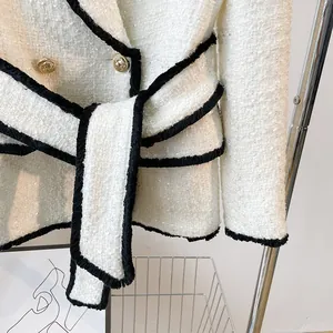White tweed jacket with black trim, waist belt, and gold buttons, urban chic style.