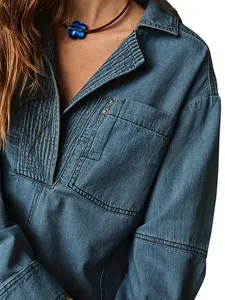 Gros plan d'une veste en jean bleue avec col en V plissé et détails de poche rivetée