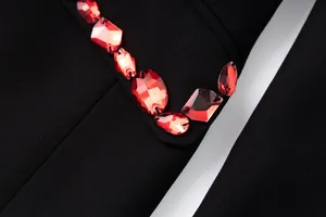 Close-up detail of sparkling red faceted crystal beads on black luxury blazer lapel edge.
