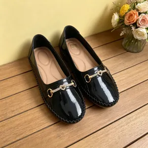 Detalle de mocasines de charol negro con hebilla de bocado de corazón sobre madera.