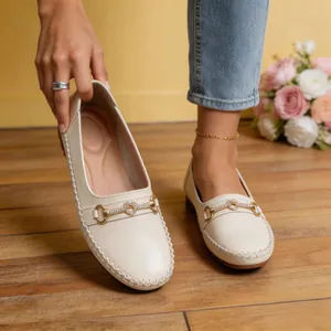 Primer plano de elegantes mocasines crema con hebilla decorativa de corazón dorado y cristales.